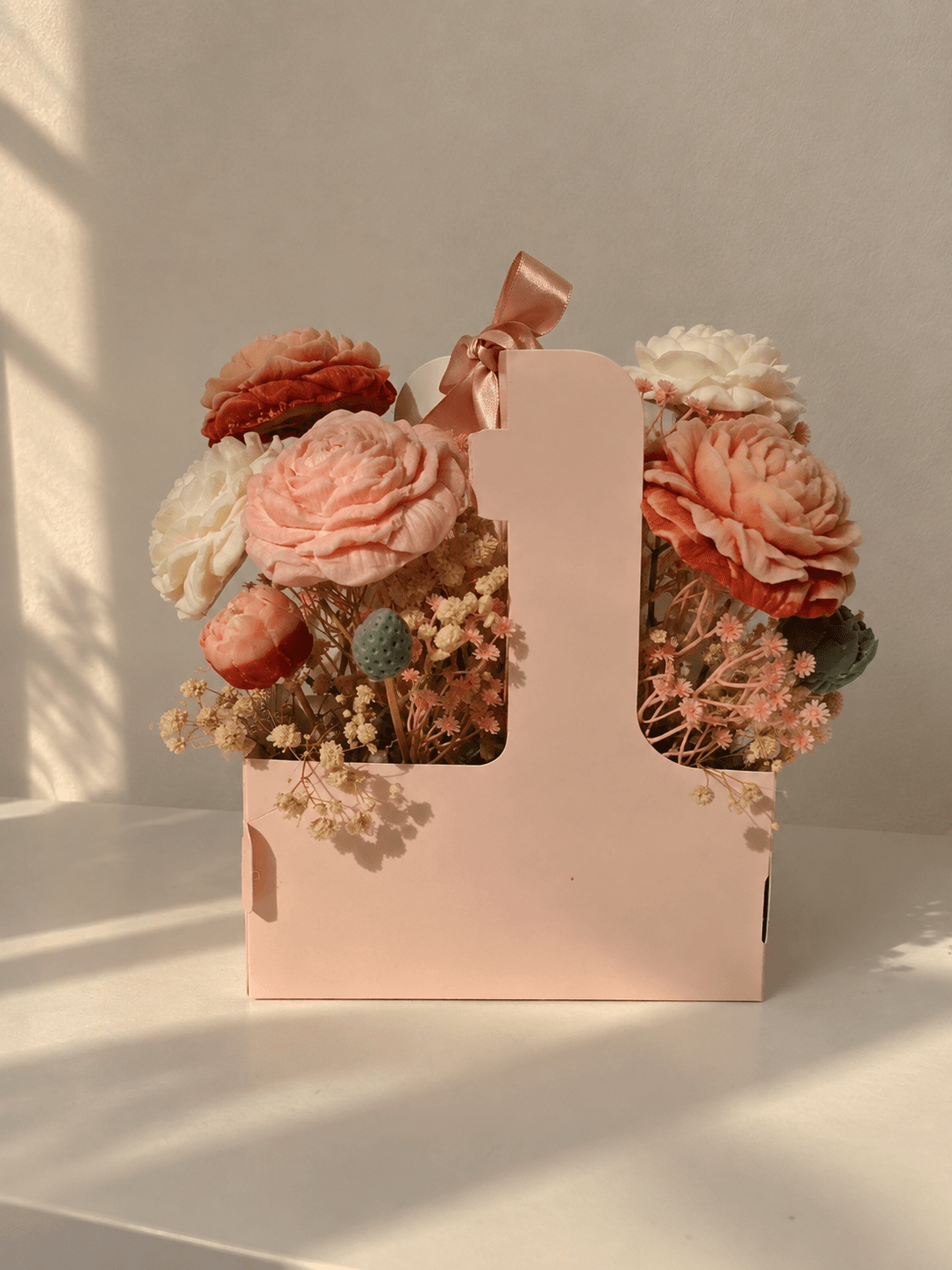 Blush, peach and ivory sculpted flower candles arranged in a pink handled gift carrier